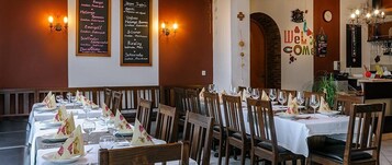 Um restaurante com várias mesas preparadas para refeições, com um cardápio na parede e um letreiro de 'Bem-vindo'.