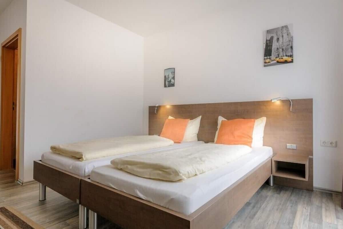 A modern bedroom with a wooden bed frame, two pillows, a bedside table, and a wall-mounted light.