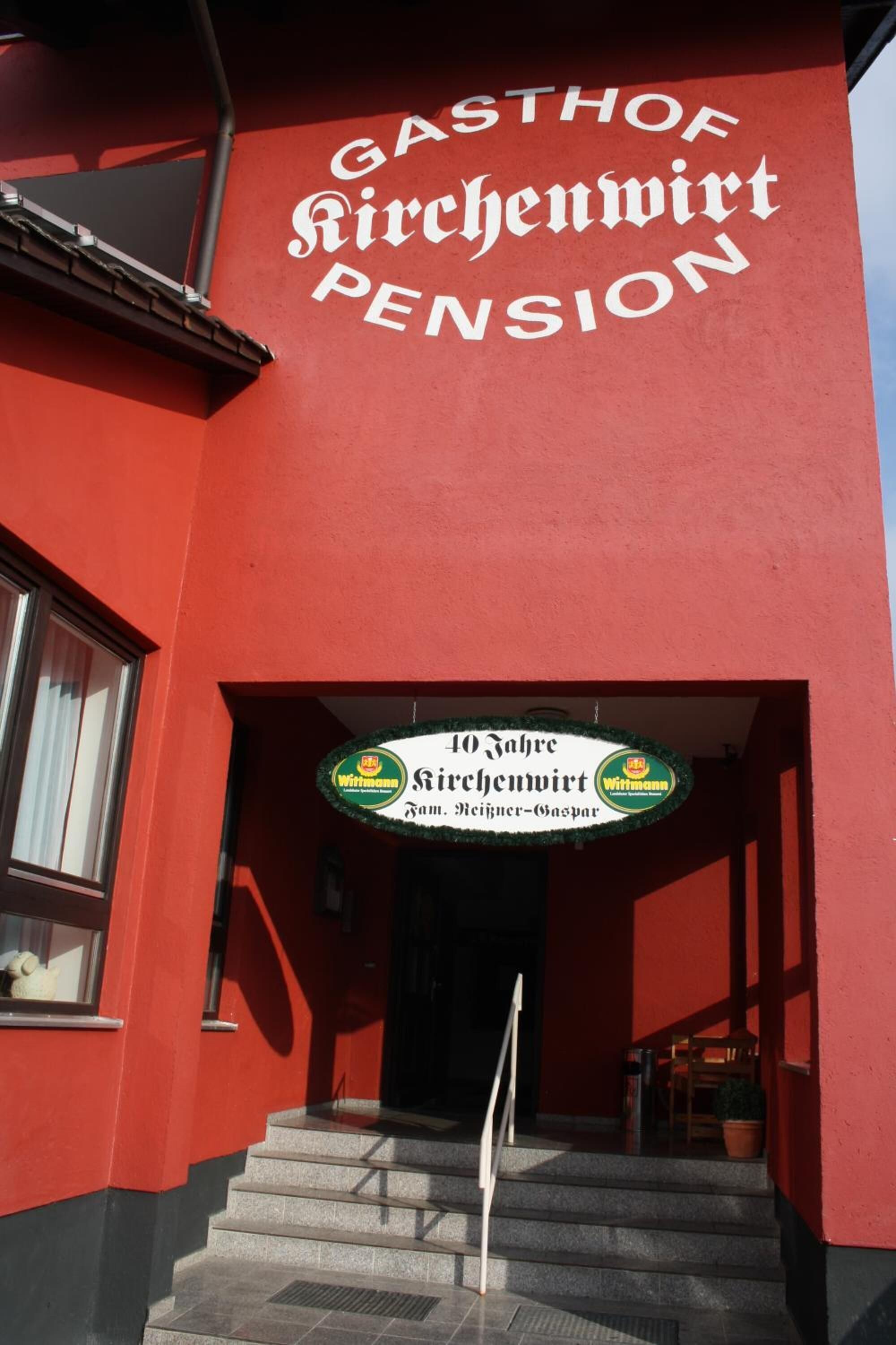 A building with a red facade and a sign that reads "GASTHOF RICHENVIRT PENSION".