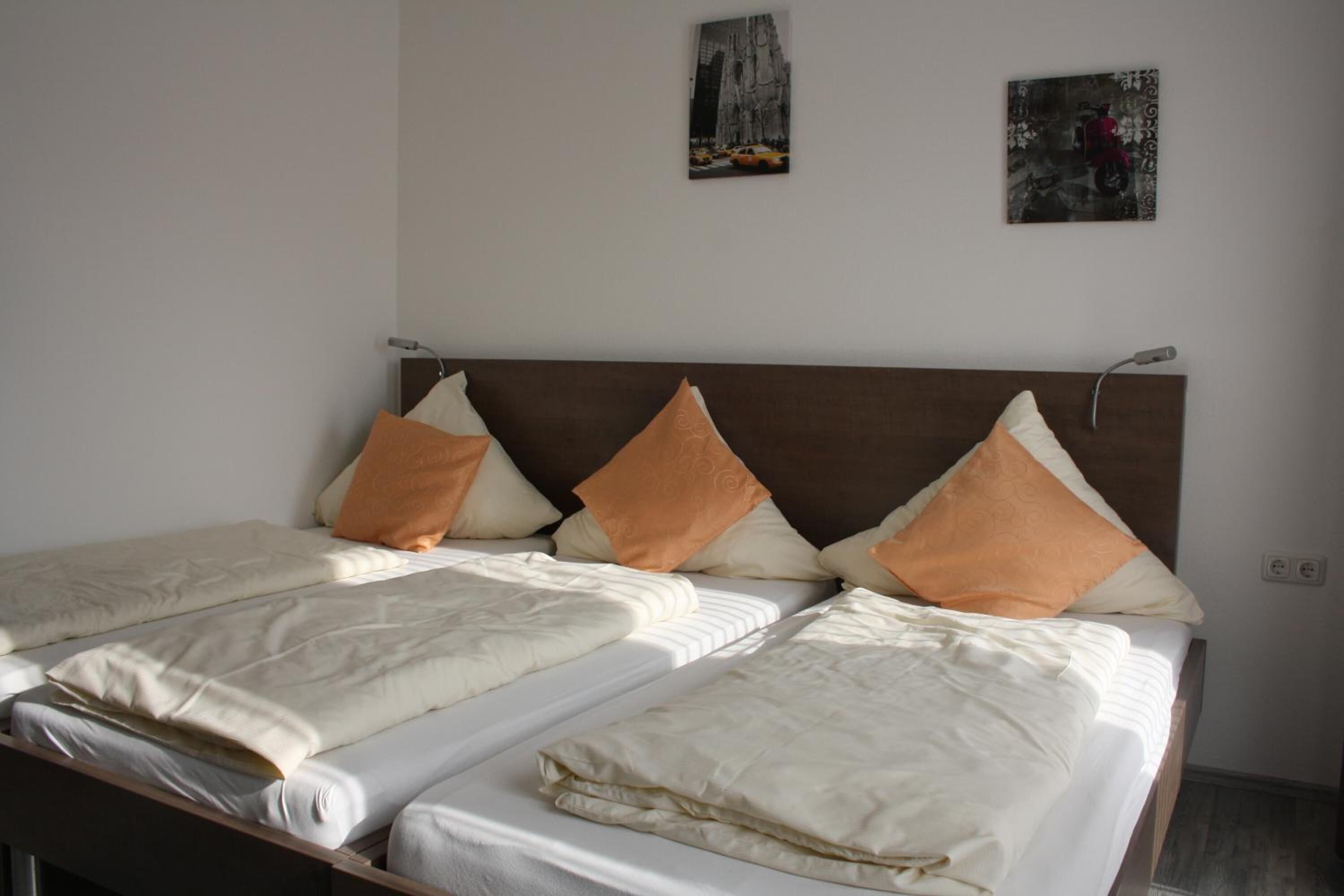 Un lit double avec deux oreillers, une tête de lit en bois et un mur blanc orné de deux tableaux encadrés.