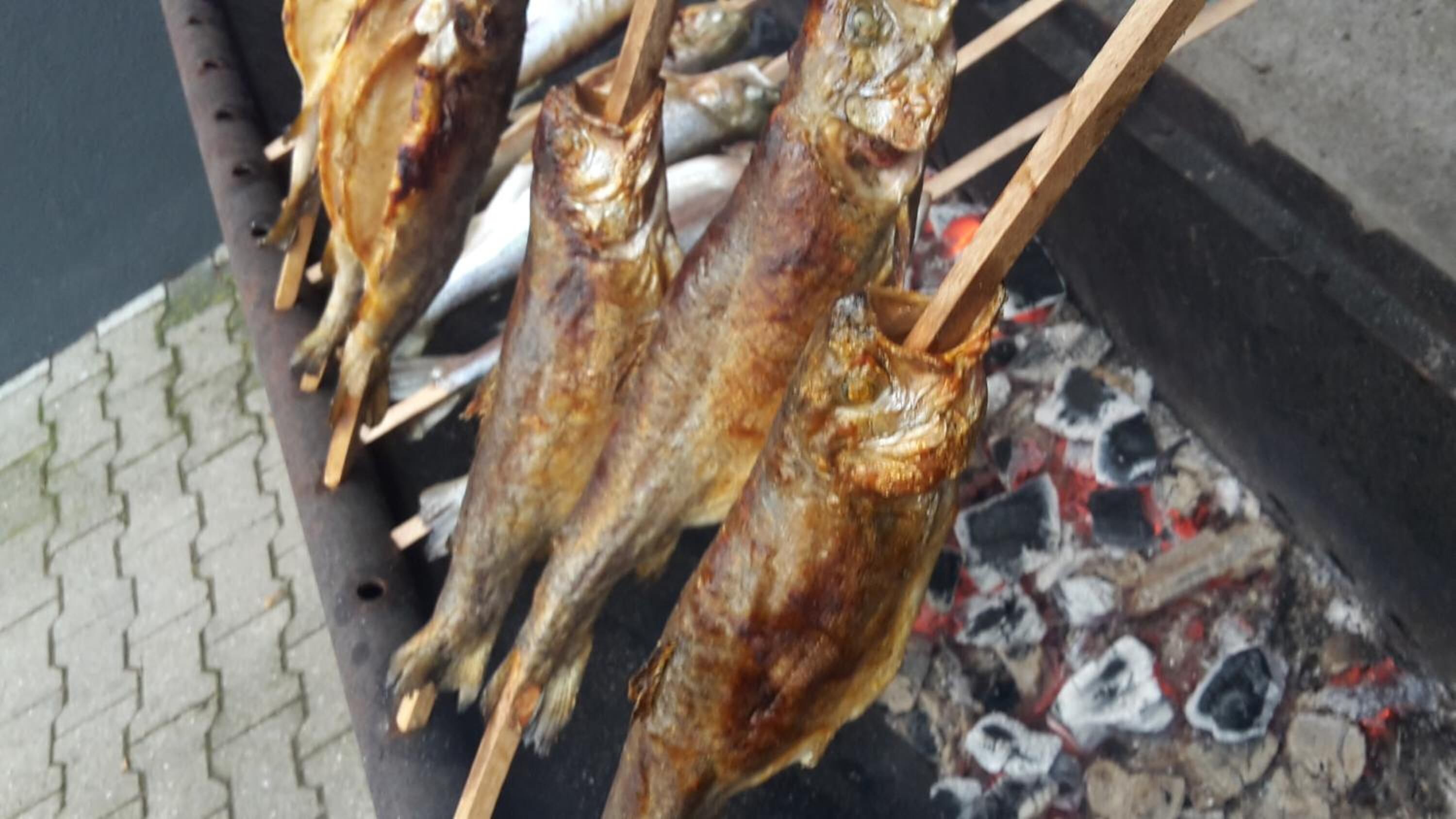 Mehrere gegrillte Hähnchen am Spieß über offenem Feuer.
