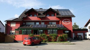A red building with solar panels on the roof, labeled "KIRCHENWIRT PENSION." - Gasthof-Pension Kirchenwirt (Niederaichbach)