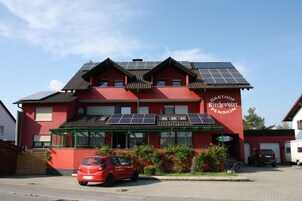 A red building with solar panels on the roof, labeled "KIRCHENWIRT PENSION."