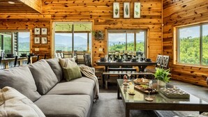 Un acogedor interior de cabaña con paredes de madera, una zona de comedor y ventanas amplias con vistas a las montañas.