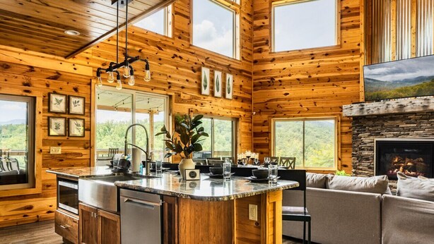 Interior de una cabaña de madera con una isla de cocina, comedor y chimenea.