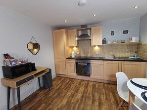 A compact kitchen with wooden cabinets, a microwave, a sink, and a small dining area. - George Hudson Ground floor apartment with parking (York)
