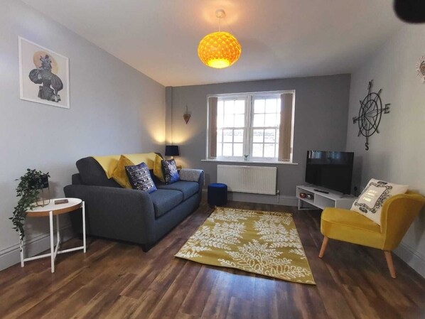 A living room with a sofa, a yellow armchair, a TV, and a large window. - George Hudson Ground floor apartment with parking (York)