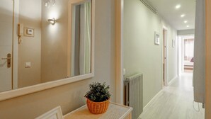 A hallway with a large mirror, a wicker basket with a plant, a radiator, and a door with a phone. - La Gioia 1 by Hello Homes Sitges (Sitges)