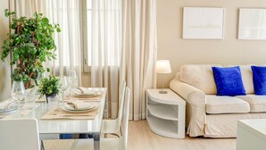A modern living room with a dining area. There is a sofa with blue cushions, a table set for dining, and a potted plant. - La Gioia 1 by Hello Homes Sitges (Sitges)