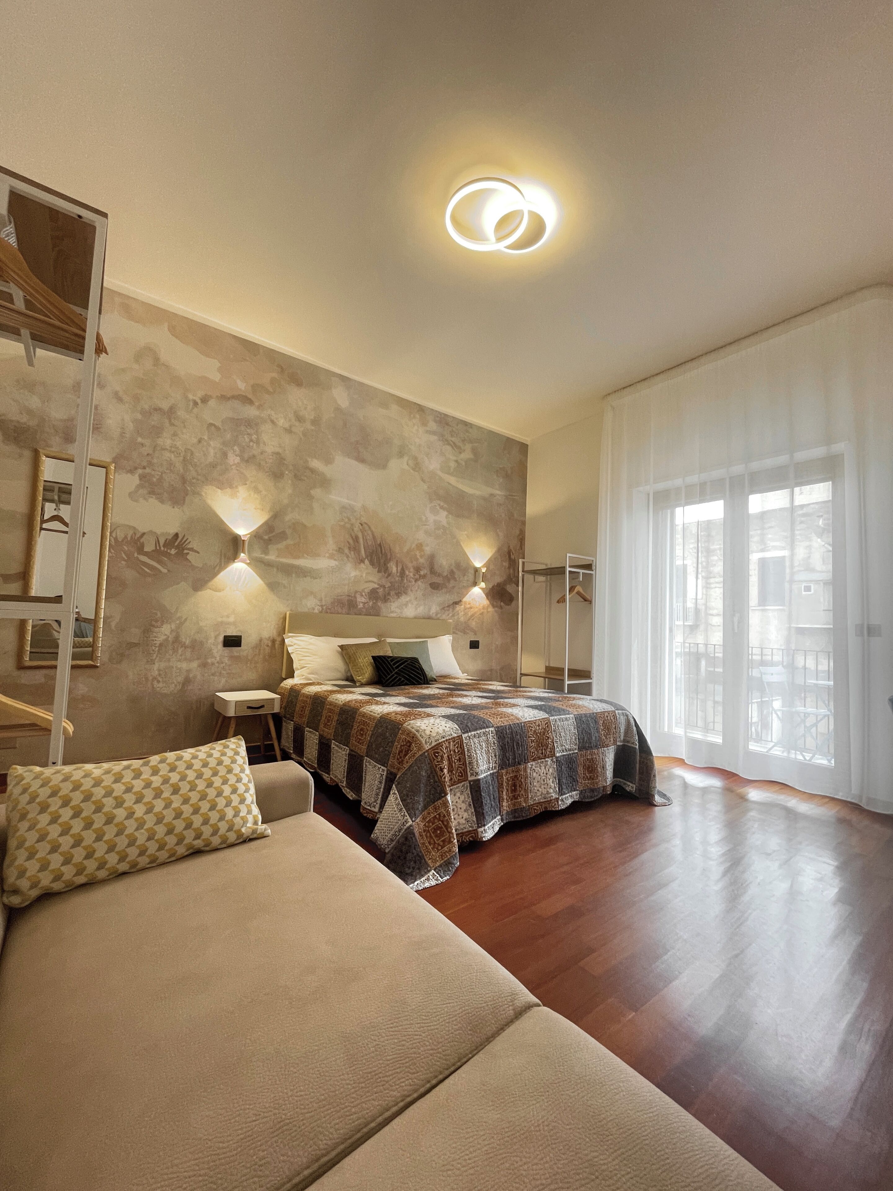 A modern bedroom with a large bed, a sofa, and a view of the outdoors through a large window.