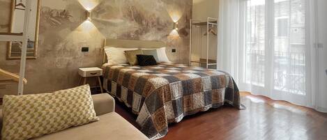 A modern bedroom with a large bed, a sofa, and a view of the outdoors through a large window.