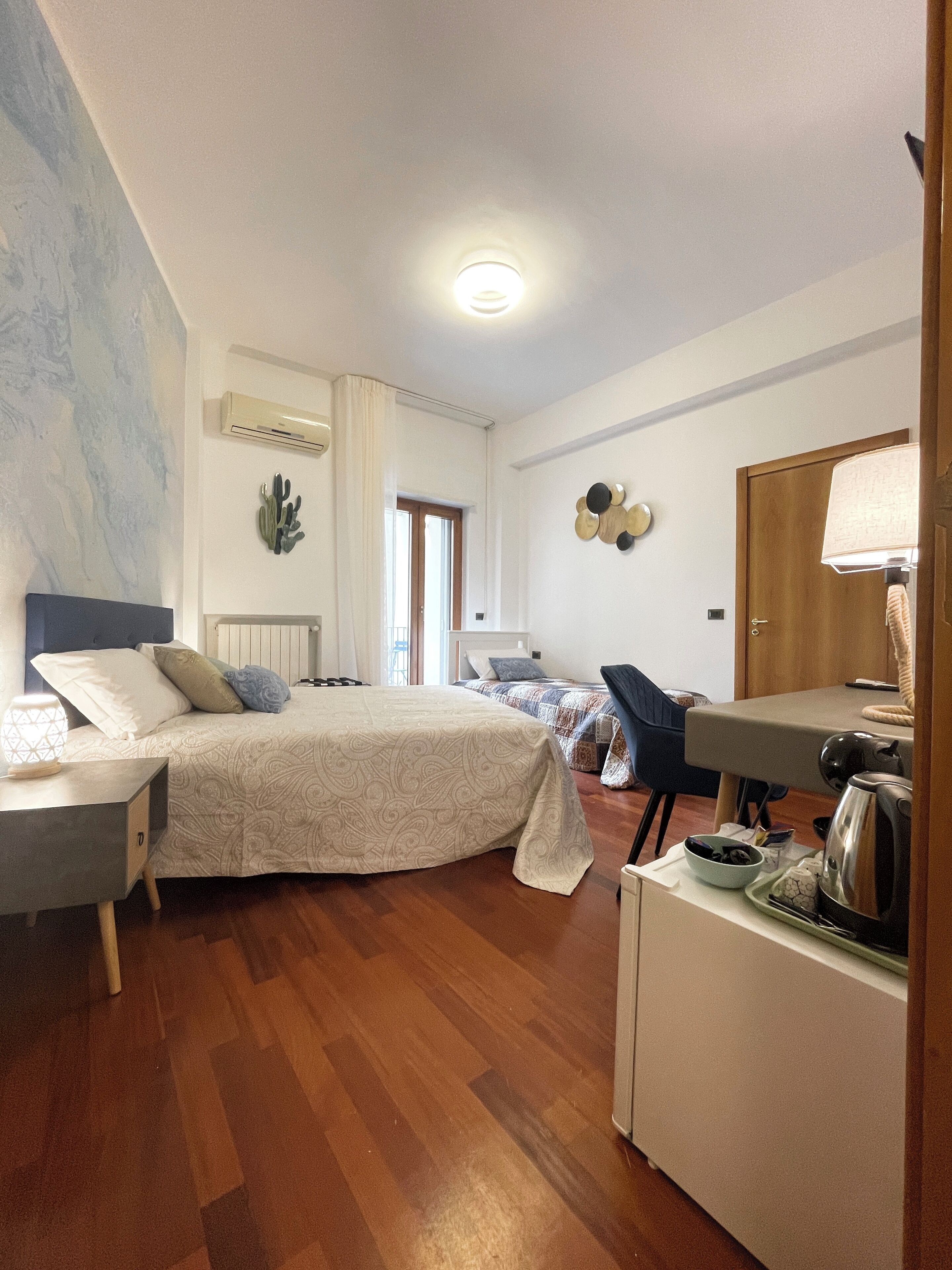 A bedroom with a bed, bedside table, lamp, and a small kitchenette area.
