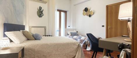 A bedroom with a bed, bedside table, lamp, and a small kitchenette area.