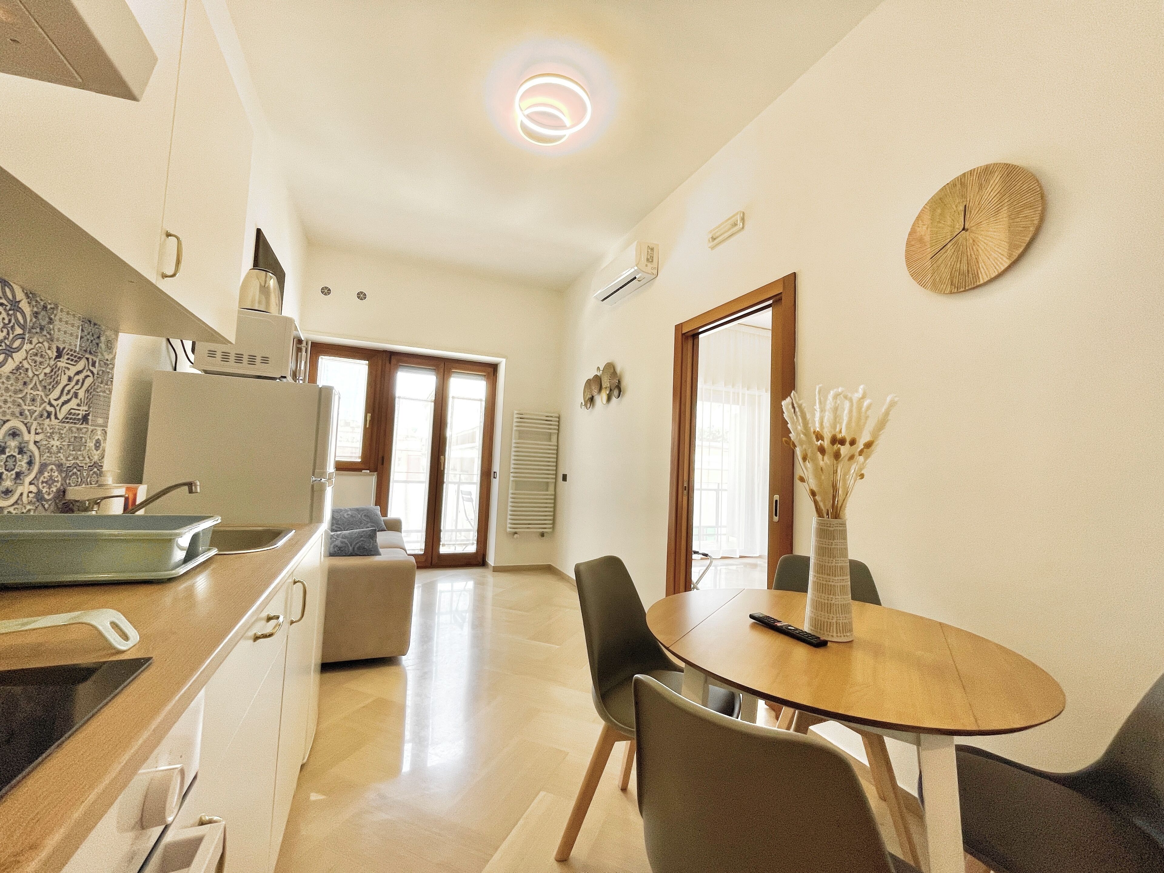 A modern kitchen with a dining area, featuring a wooden table, chairs, and a vase with dried flowers.