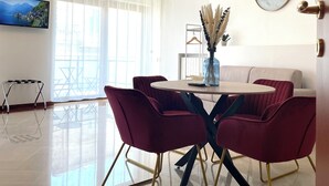 A modern living room with a dining area, featuring a large window, a mounted TV, and a decorative clock. - Dimore del Sud (Trani)