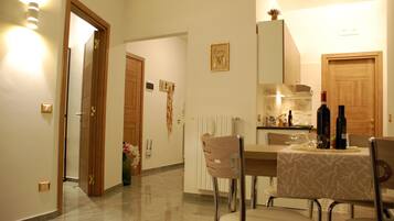 A dining area with a table set for four, a kitchen in the background, and a wooden door leading to another room.