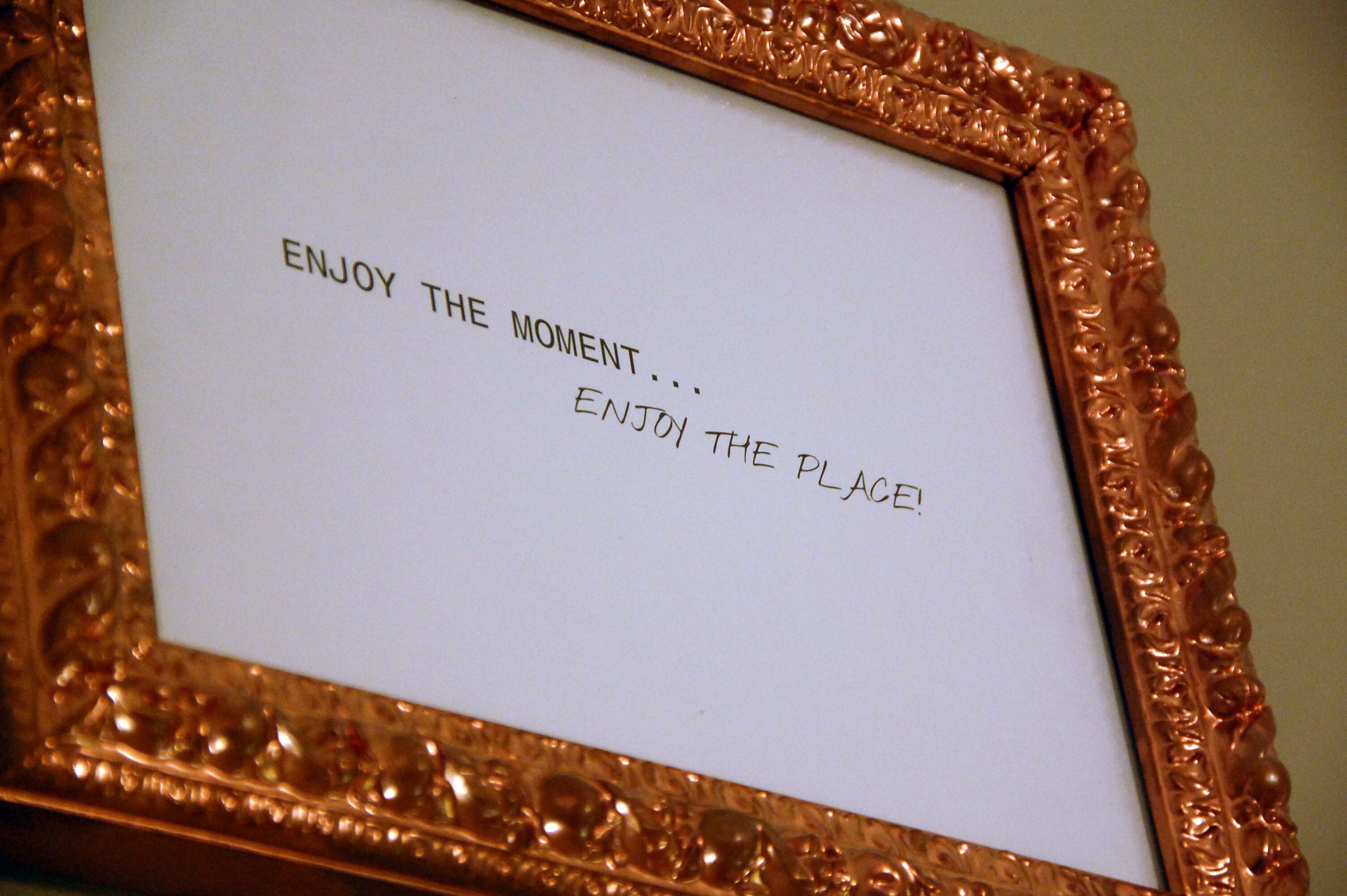 A framed sign with the text "ENJOY THE MOMENT... ENJOY THE PLACE!"