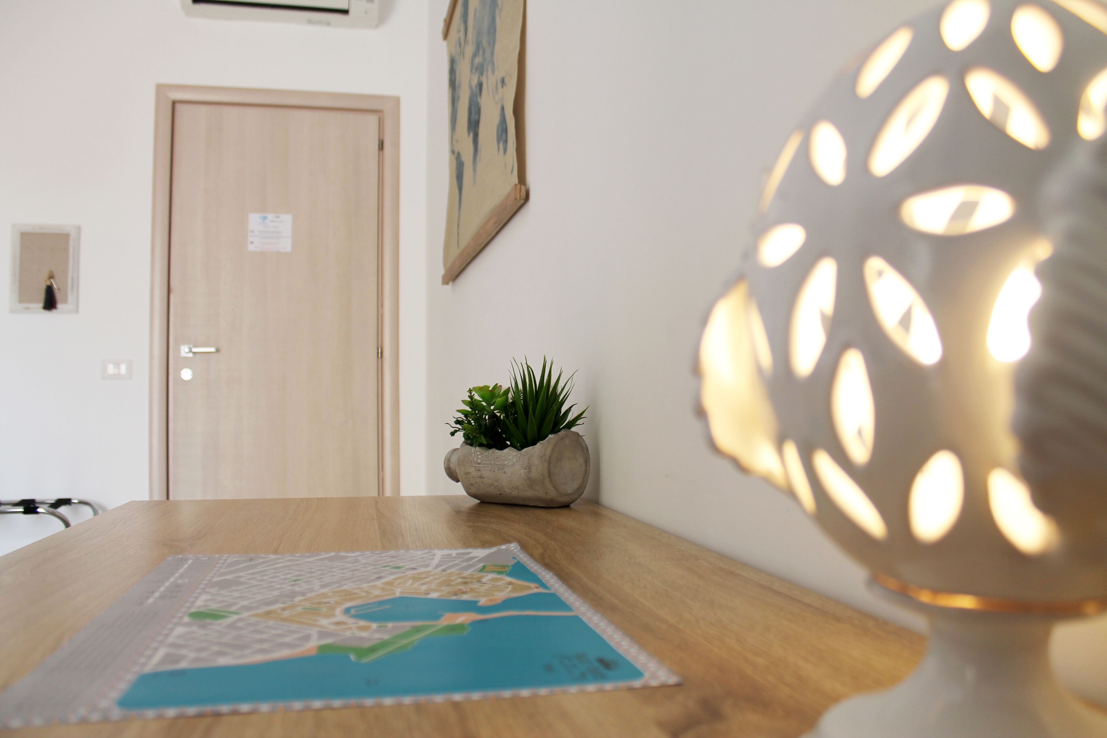 Une table en bois, sur laquelle on trouve une carte, une plante en pot et une lampe avec un abat-jour à motifs.