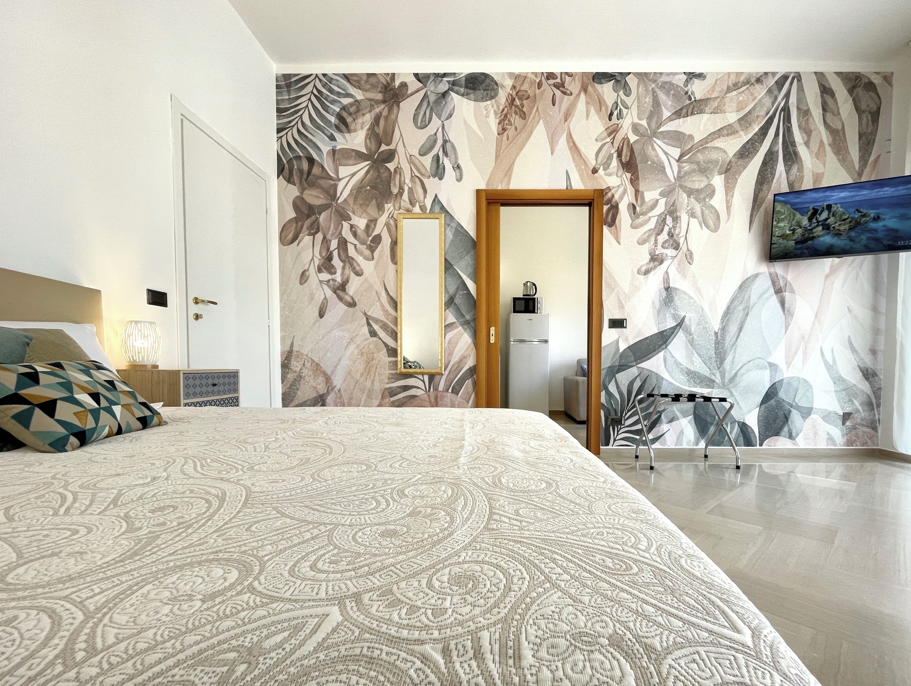 Une chambre à coucher avec une couvre-lit à motifs, un grand miroir et un téléviseur fixé au mur.