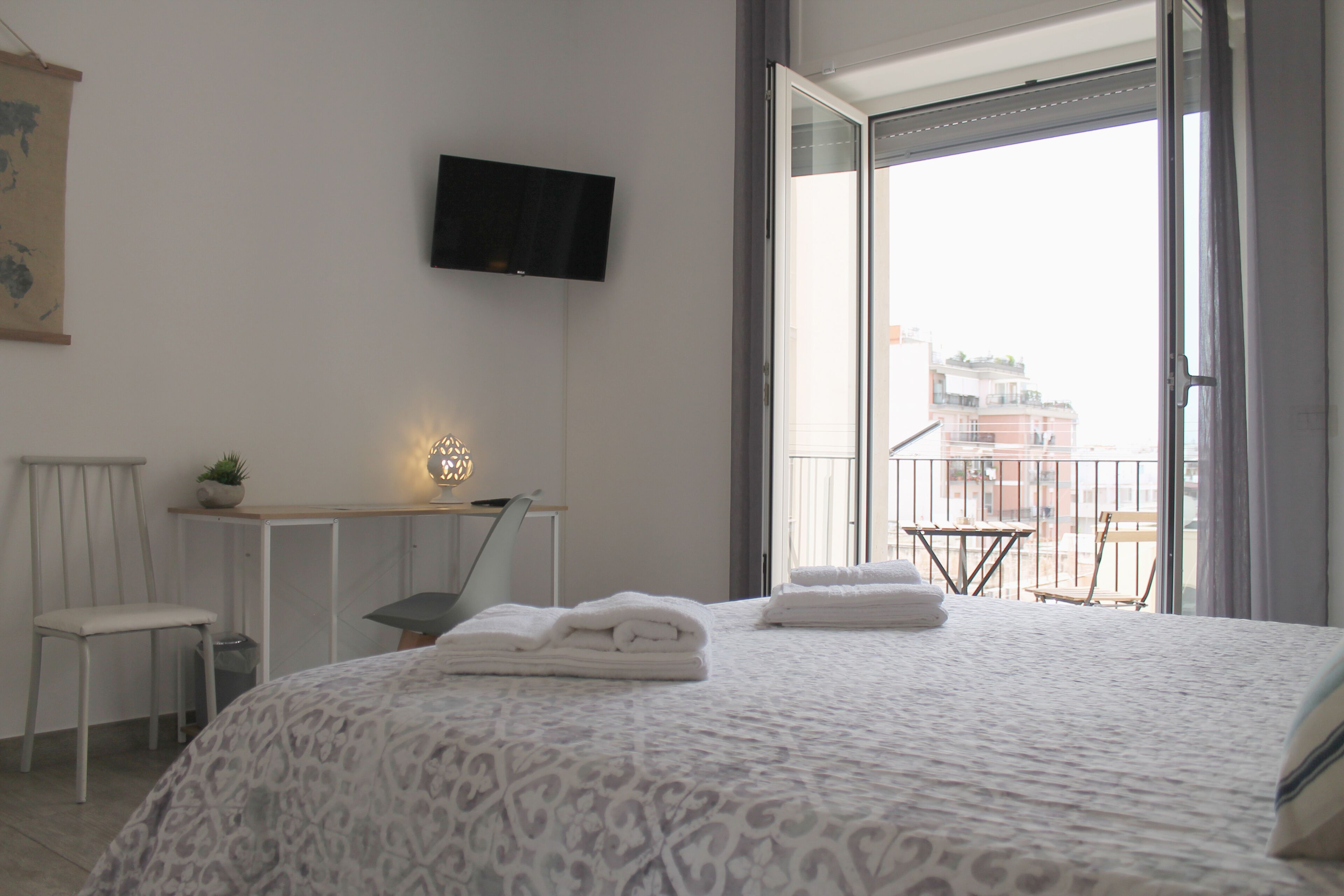 Une chambre d’hôtel comprenant un lit, un bureau, une chaise, une télévision et un balcon avec vue sur les immeubles.