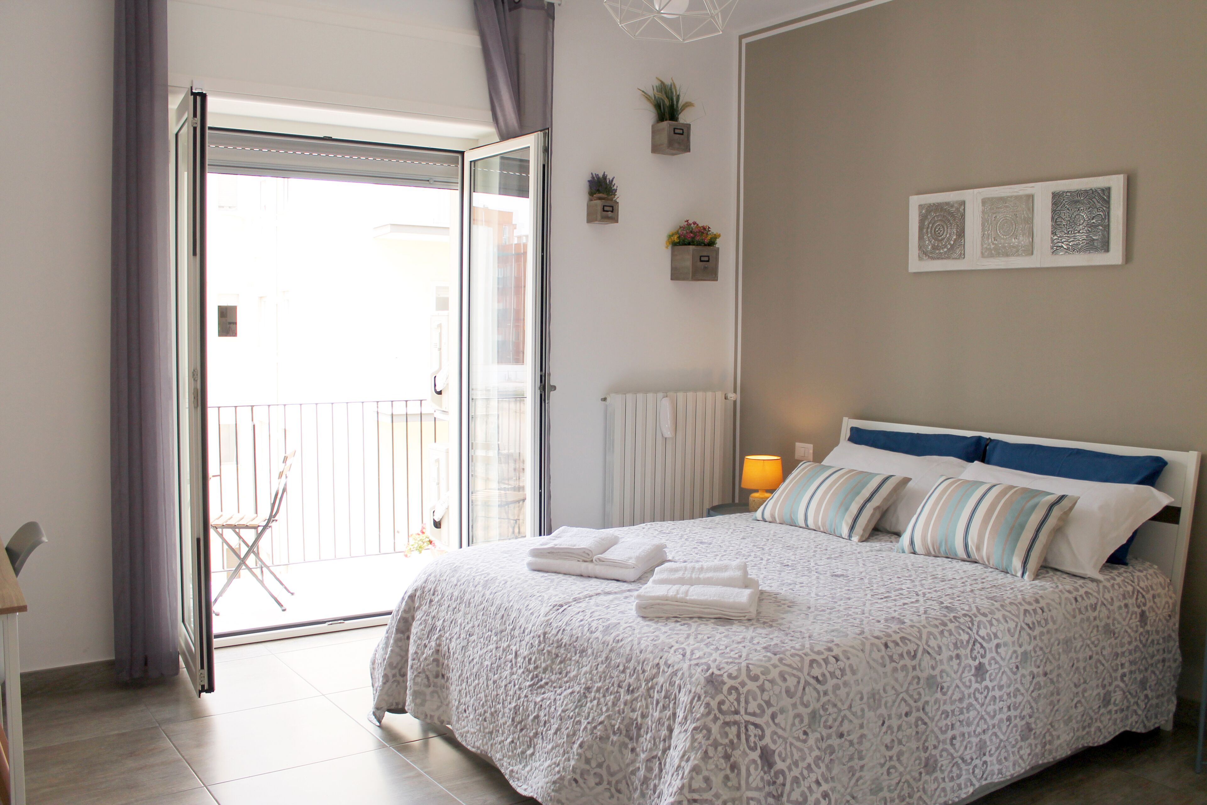 A bedroom with a bed, a sliding glass door to a balcony, and a small potted plant on the wall.