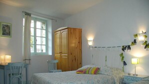 A bedroom with two beds, a wooden wardrobe, a desk with a chair, and a window with curtains. - Le Chambellan (Coux-et-Bigaroque-Mouzens)