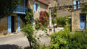 A narrow stone pathway flanked by traditional stone buildings with blue shutters and a hanging flower basket. - Le Chambellan (Coux-et-Bigaroque-Mouzens)