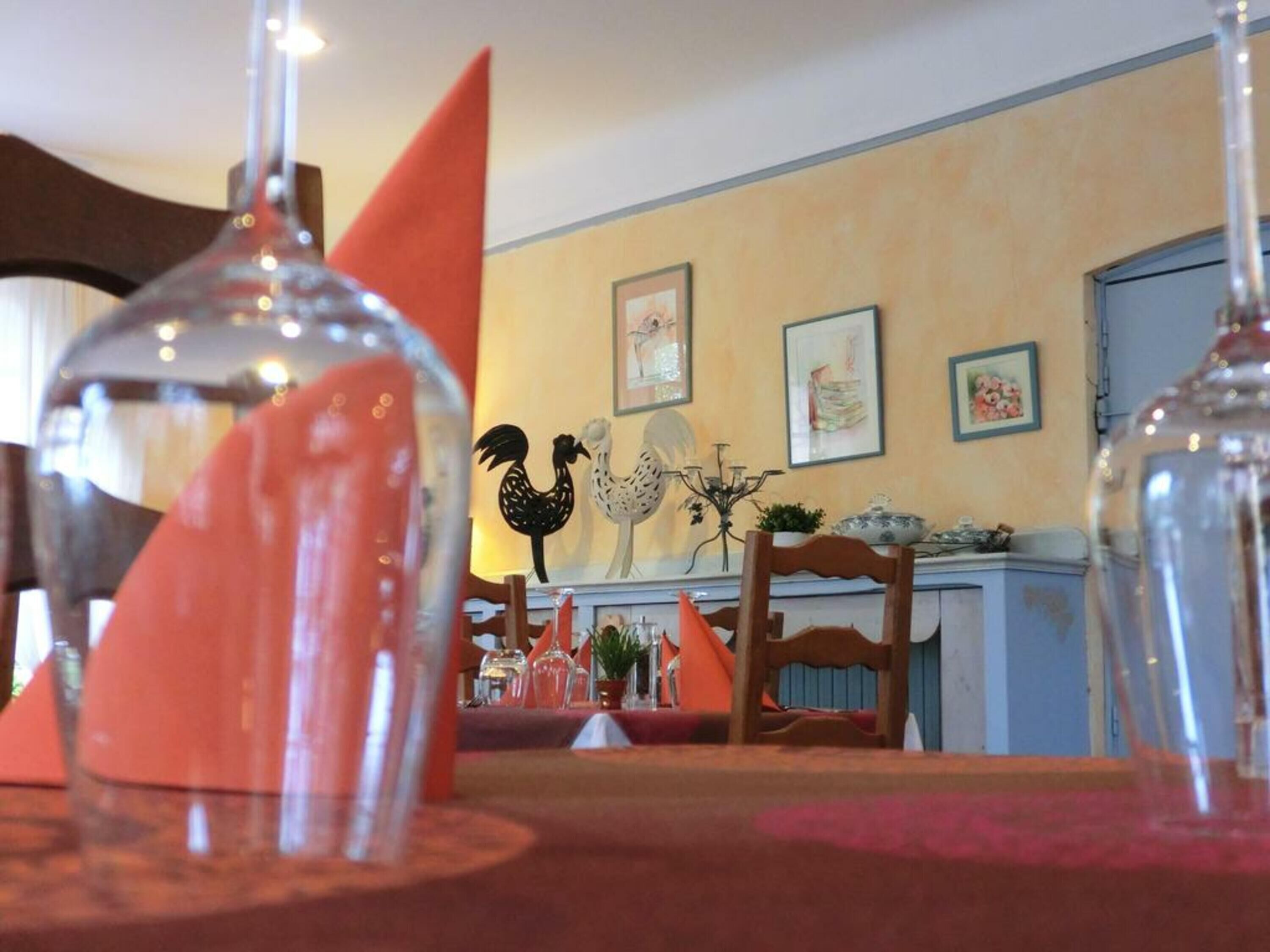 A dining area with a table set for two, featuring a clear glass vase and a red napkin.