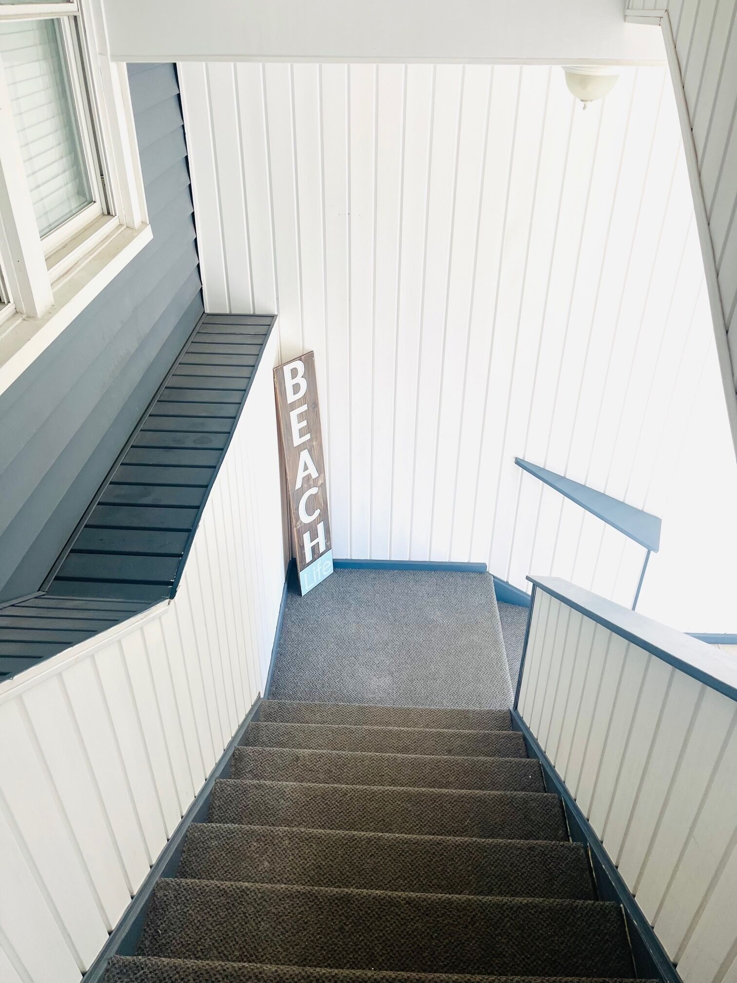 Un escalier orné d’une enseigne en bois sur laquelle on peut lire « BEACH Life » et qui offre une vue sur un mur extérieur blanc.