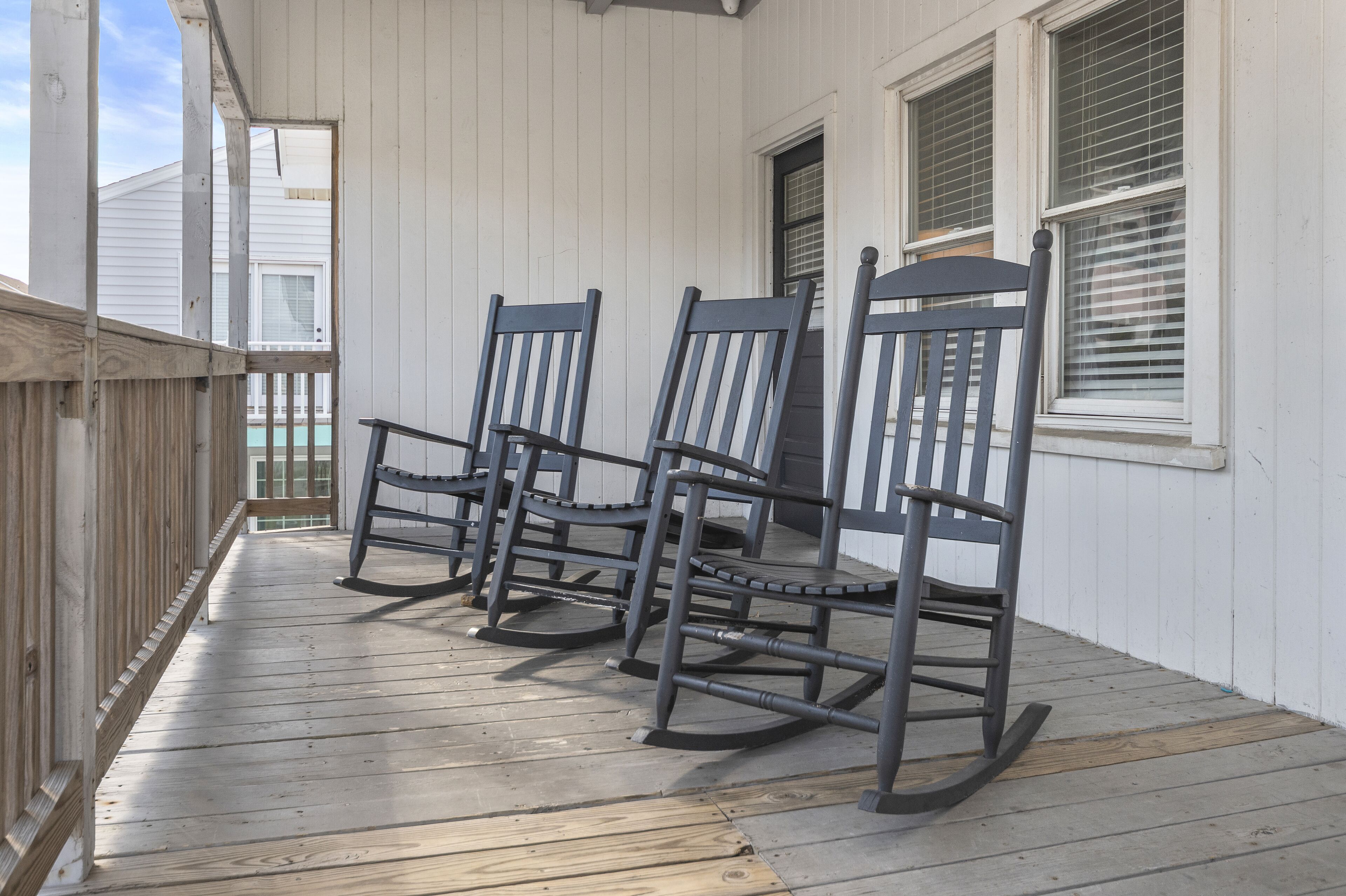 A wooden porch with three rocking chairs and a wooden railing.