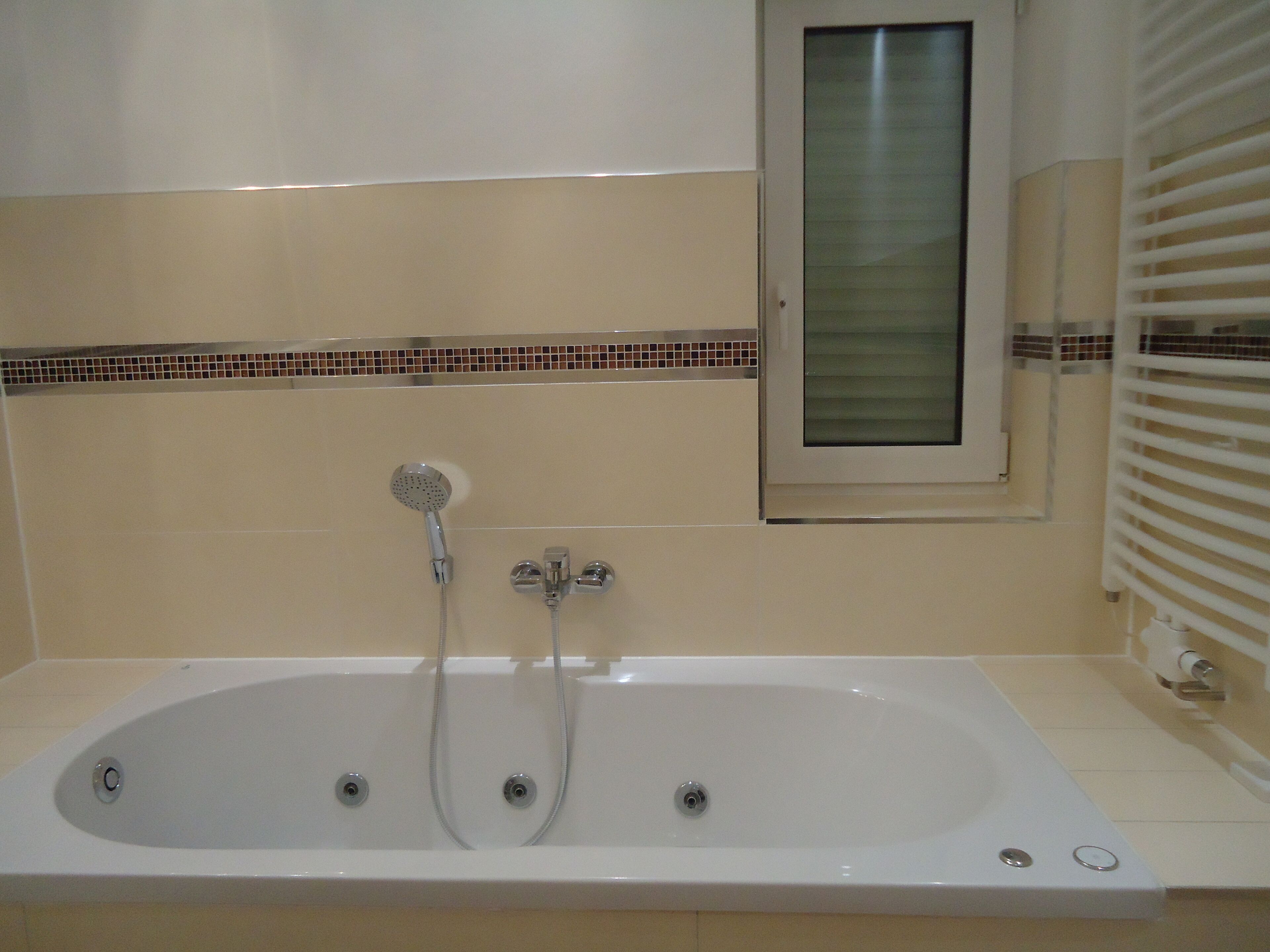 A bathroom with a large bathtub, a showerhead, and a window with blinds.