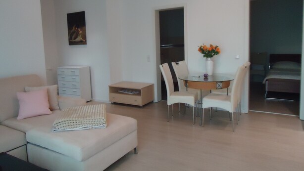 A modern living room with a sofa, a dining table with chairs, a small cabinet, and a painting on the wall. - Quality vacation rental in Berlin-Kaulsdorf (Bezirk Marzahn-Hellersdorf)