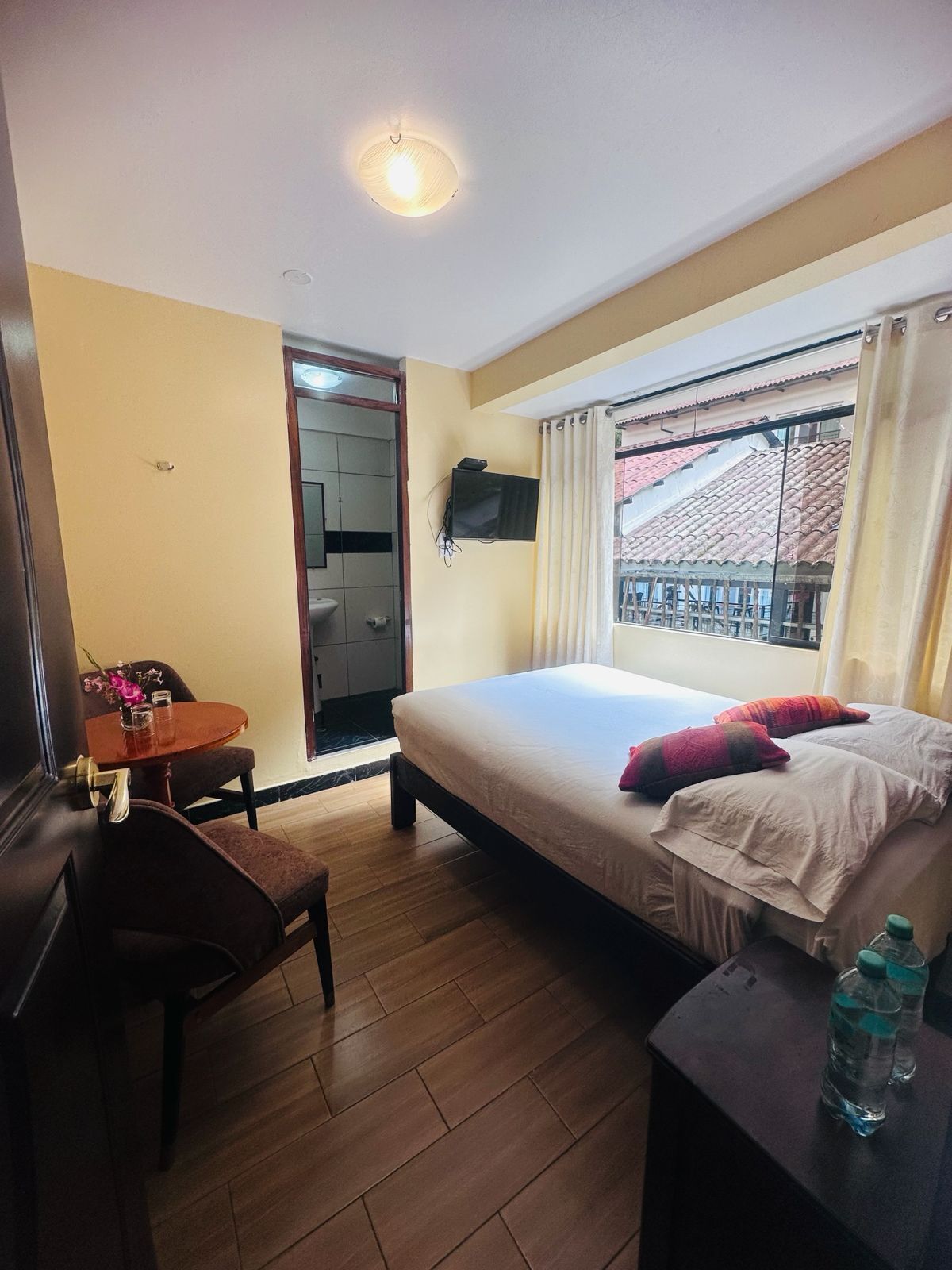 Una habitación de hotel con cama, escritorio con silla, televisor y ventana con cortinas.