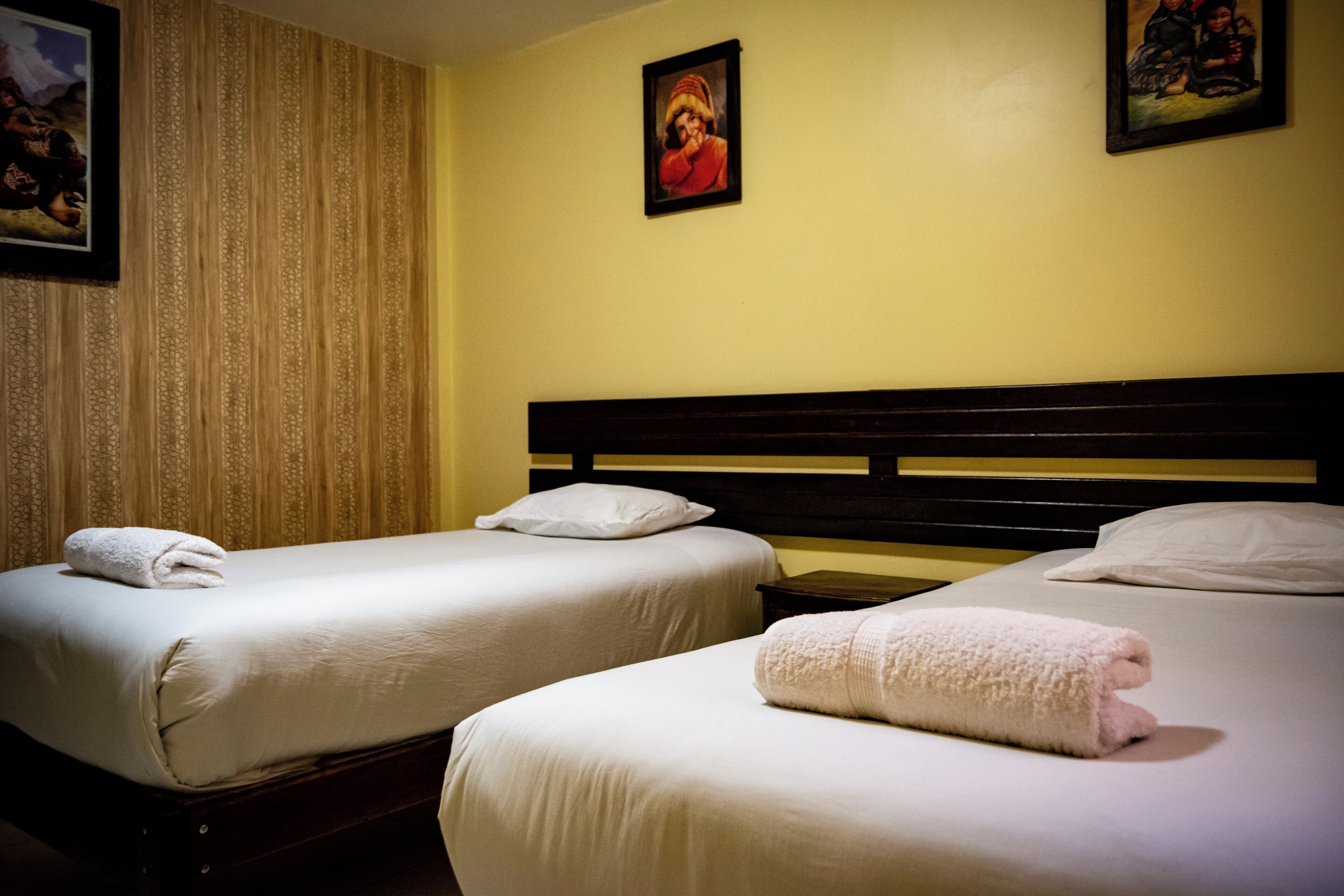 Two single beds with white linens and towels, a wooden headboard, and a patterned curtain.