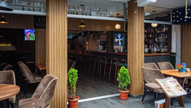 Un área de bar moderna con detalles de madera, taburetes y plantas en macetas.