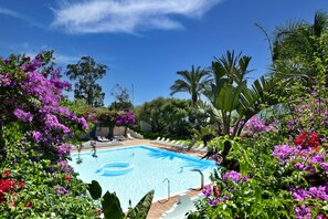 A swimming pool surrounded by lush greenery and purple flowers. - Arbatax Park Resort - Ville del Parco by Falkensteiner (Tortoli)