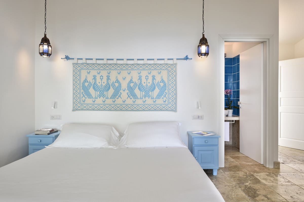 A bedroom with a bed, two nightstands, a wall-mounted artwork, and a bathroom visible through an open door.