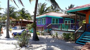 A beachside resort with colorful buildings, a sandy area with lounge chairs, and palm trees. - Coco's Beachfront Cabanas (Placencia)