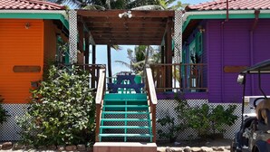 A staircase leading to a covered area with a wooden railing, surrounded by colorful buildings and greenery. - Coco's Beachfront Cabanas (Placencia)