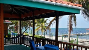 A covered outdoor area with blue chairs and a table, overlooking a beach with palm trees and the ocean. - Coco's Beachfront Cabanas (Placencia)