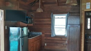 A compact kitchen with wooden walls, a refrigerator, a microwave, and a sink. - Coco's Beachfront Cabanas (Placencia)