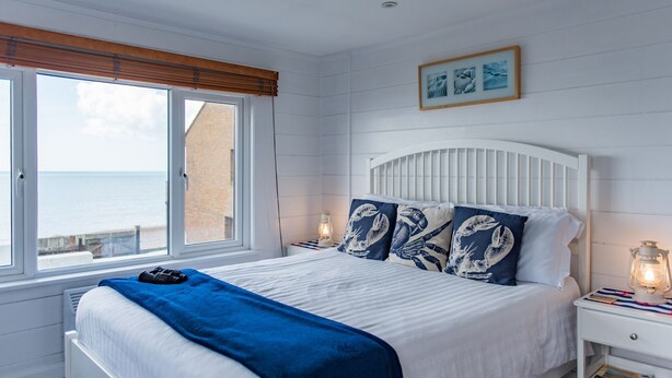 A bedroom with a bed, a nightstand, a lamp, and a window with a view of the sea. - Pebbles by Bloom Stays - sleeps 2 with the most amazing sea views! (Folkestone)