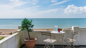 A balcony with a potted plant, two chairs, and a table with a glass and a red cup. - Pebbles by Bloom Stays - sleeps 2 with the most amazing sea views! (Folkestone)