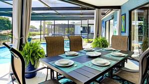 Un espace extérieur aménagé pour les repas, avec vue sur la piscine, un patio couvert et des chaises de salle à manger.