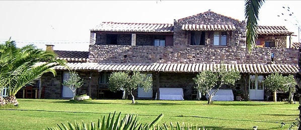 A stone building with a tiled roof, multiple windows, and a well-maintained lawn with palm trees.