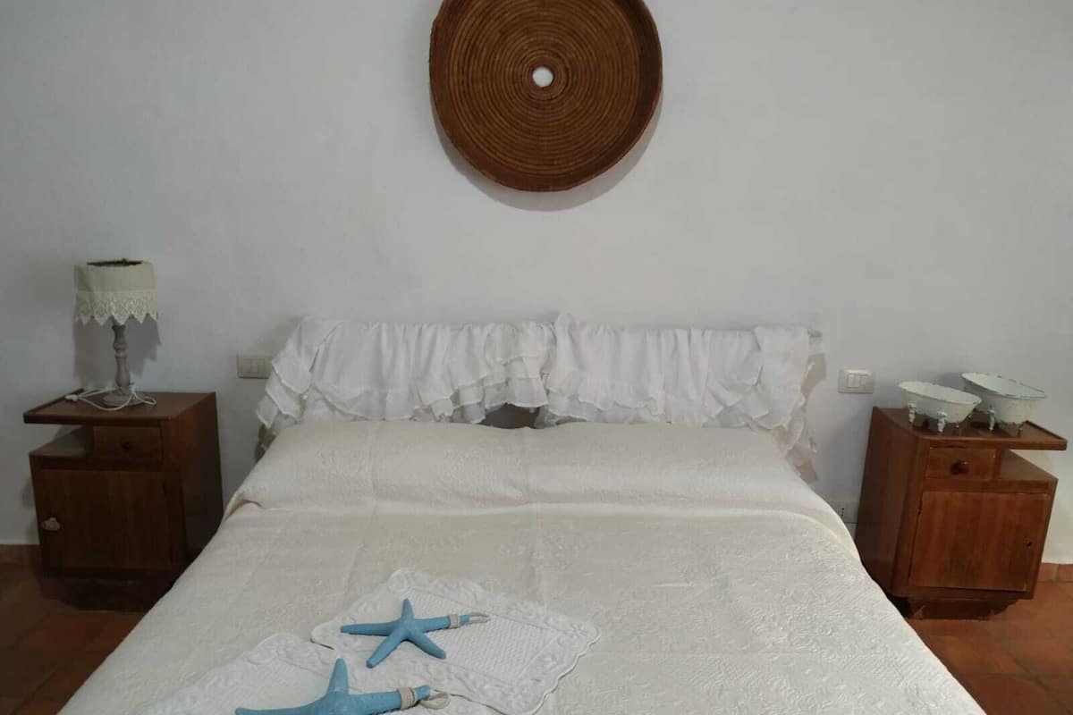 A bedroom with a bed, two nightstands, a wall hanging, and two starfish decorations.