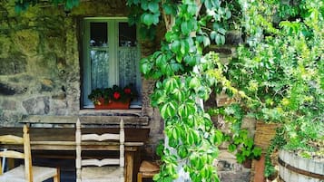 Un edificio de piedra rústica con un banco de madera y una mesa bajo un tejado de baldosas.