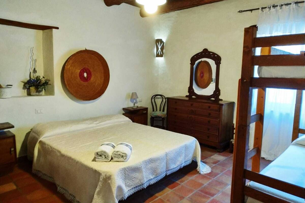A bedroom with a bed, a dresser, a mirror, a wall-mounted clock, and a window with curtains.
