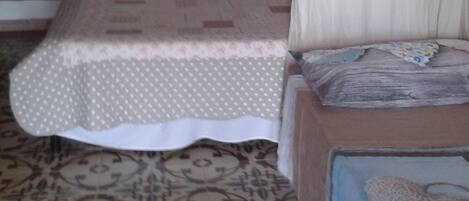 A bedroom with a bed, a wooden wardrobe, a painting on the wall, and patterned floor tiles.