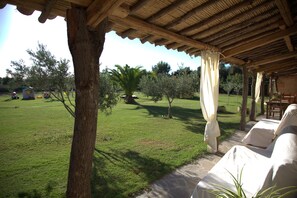 A covered outdoor seating area with a view of a grassy field and trees.